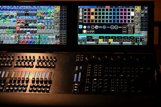 A detailed view of a lighting control panel featuring multiple digital displays and buttons, actively being used during a rehearsal at a theater venue.