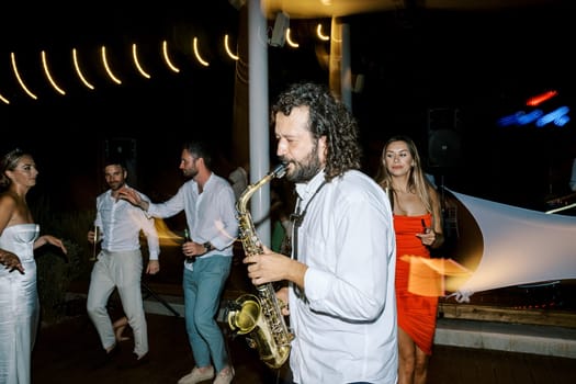 Saxophonist plays saxophone among dancing guests at wedding. High quality photo