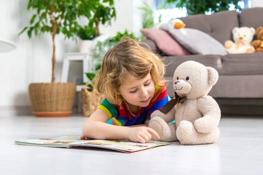 Child reading a book at home with a teddy bear at home. Selective focus. kid.