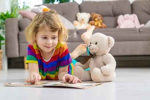 Child reading a book at home with a teddy bear at home. Selective focus. kid.