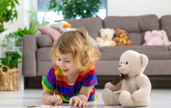 Child reading a book at home with a teddy bear at home. Selective focus. kid.