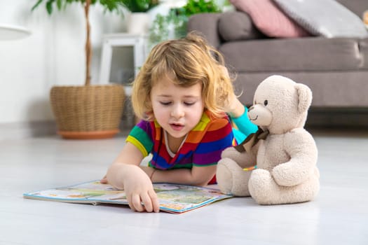 Child reading a book at home with a teddy bear at home. Selective focus. kid.