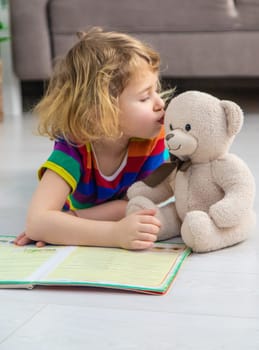 Child reading a book at home with a teddy bear at home. Selective focus. kid.