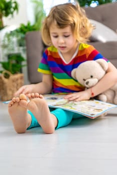 Child reading a book at home with a teddy bear at home. Selective focus. kid.