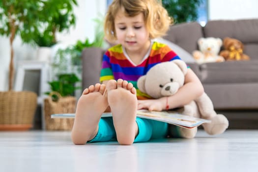 Child reading a book at home with a teddy bear at home. Selective focus. kid.