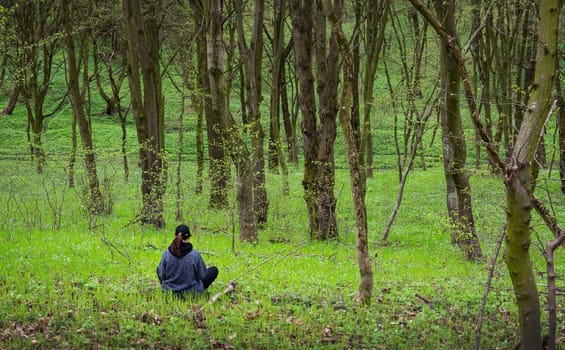 A woman sits serenely in a sun-dappled spring forest, enjoying the tranquil atmosphere.