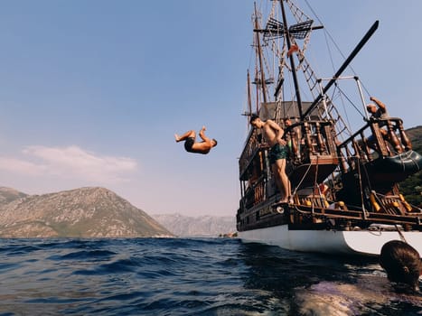Young men jump into the sea from the deck of a wooden sailing yacht. High quality photo