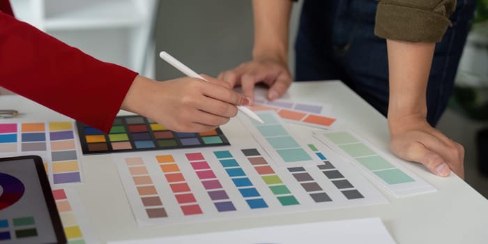 Two creative minds work together at a desk, selecting color shades and interacting around design palettes. The scene emphasizes teamwork in the art of graphic design.