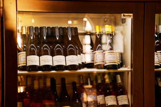 Bottles of wine stand in rows on shelves in a wine refrigerator. High quality photo