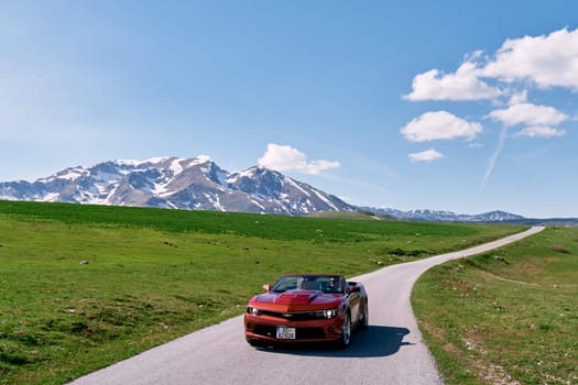 Bride and groom are driving in a red convertible along a mountain road. High quality photo