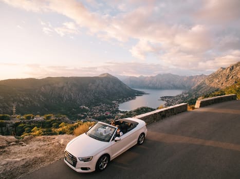 Bride and groom are driving in a convertible along a road above the Bay of Kotor. Montenegro. Drone. High quality photo