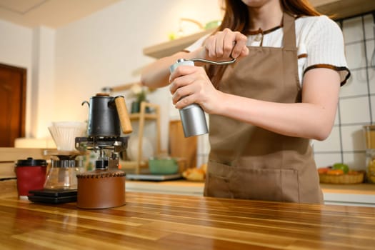 Close up of a woman using manual coffee grinder while preparing fresh coffee in a warm kitchen.