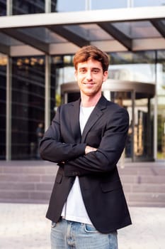 young adult man in casual suit standing looking at camera with arms crossed in front of an office building, concept of entrepreneur and business, copyspace for text