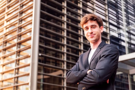 young adult man in casual suit standing looking at camera with arms crossed in front of an office building, concept of entrepreneur and business, copyspace for text
