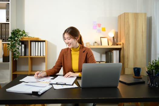 Smiling businesswoman sitting at desk with laptop, reviewing graphs and statistics.