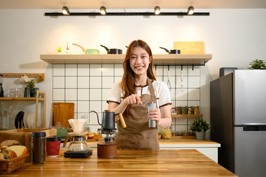 Happy woman in an apron crafting her morning coffee using traditional brewing tools in a kitchen.