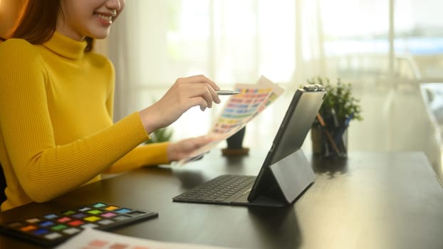Female graphic designer working with digital tablet and color swatches at creative workplace.