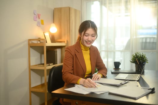 Smiling businesswoman sitting at desk with laptop, reviewing graphs and statistics.