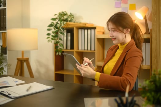 Smiling young entrepreneur wearing a brown blazer using digital tablet in stylish workplace.