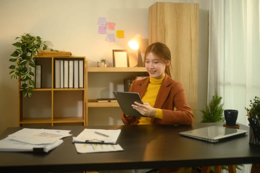 Smiling young entrepreneur wearing a brown blazer using digital tablet in stylish workplace.