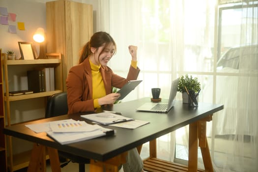 Excited young businesswoman celebrating a positive result while looking at digital tablet.
