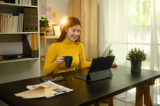 Female graphic designer working with digital tablet and color swatches at creative workplace.