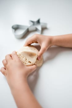Child playing with dough near star shaped cookie cutter on white surface.