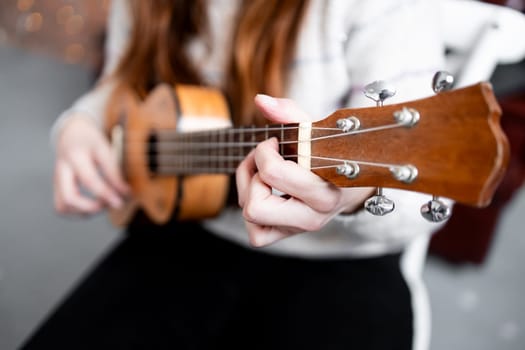 Young female playing ukulele indoors with focus on strings and hands.
