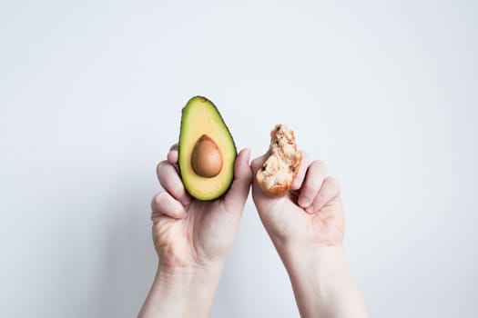 Hands holding fresh avocado and seed against white background.