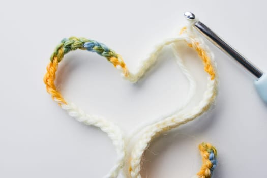 Colorful crochet hook with heart shaped yarn on white background.