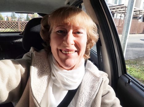 A middle-aged woman captures a lively selfie while driving on her travel excursion on a beautiful day.