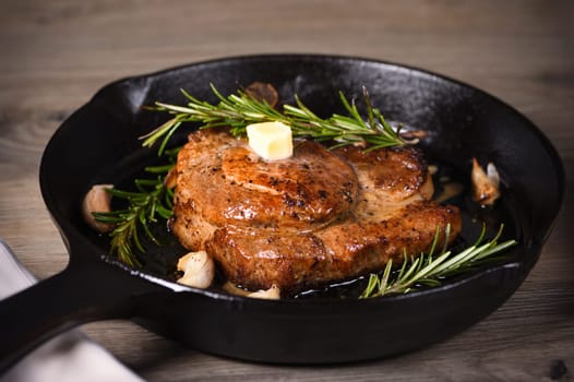 Pork cutlet on the bone in a piece of butter with garlic and rosemary in a frying pan 
