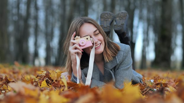 A young beautiful girl takes pictures in an autumn park using a toy camera