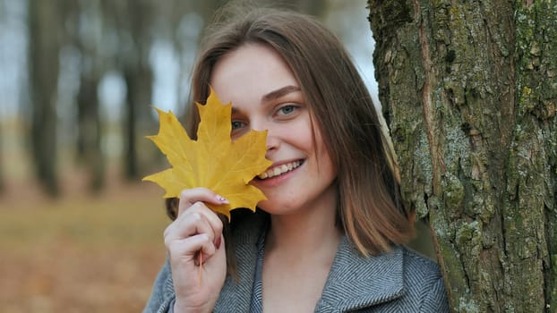 Beautiful happy woman with a smile holds an autumn yellow leaf near the face