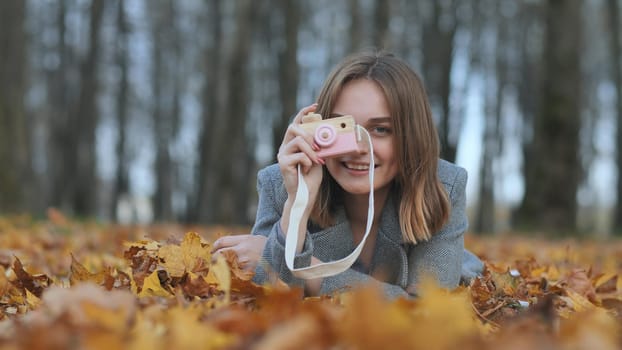 A young beautiful girl takes pictures in an autumn park using a toy camera