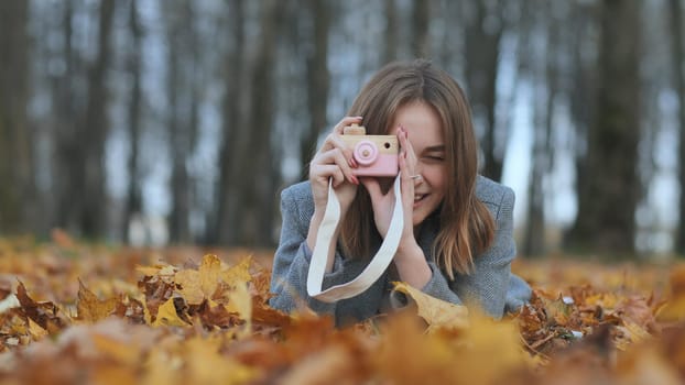 A young beautiful girl takes pictures in an autumn park using a toy camera