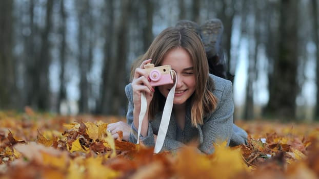 A young beautiful girl takes pictures in an autumn park using a toy camera