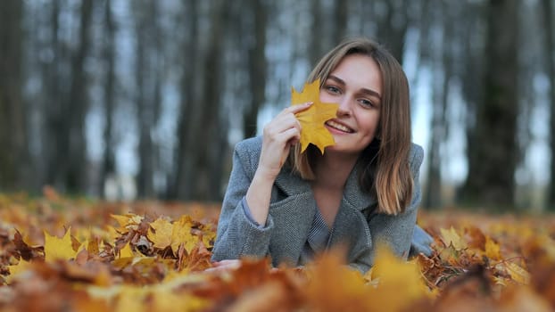 Beautiful happy young girl with a smile holds an autumn yellow leaf near the face