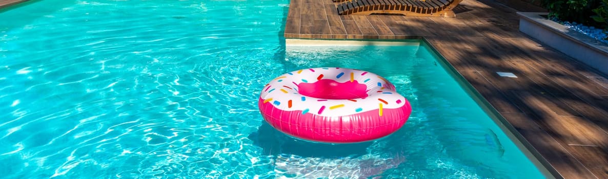Pink donut-shaped inflatable float in turquoise swimming pool with wooden deck in sunny backyard