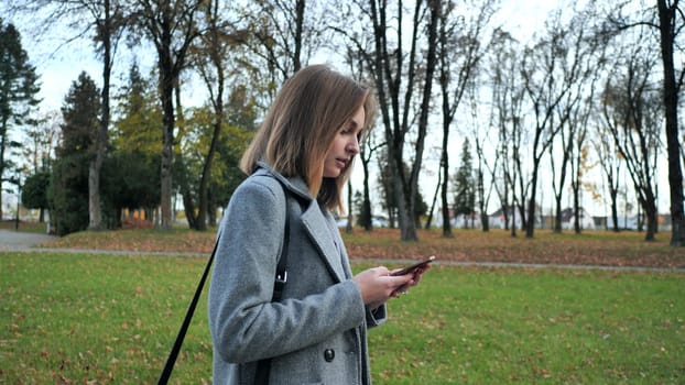 A young girl walks through the autumn park and dials a number on the phone