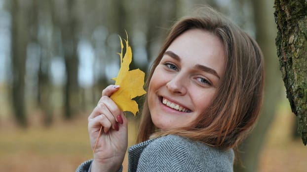 Beautiful happy woman with a smile holds an autumn yellow leaf near the face