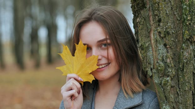 Beautiful happy young girl with a smile holds an autumn yellow leaf near the face