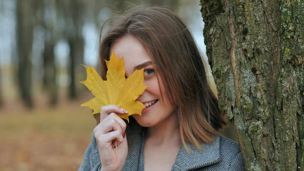 Beautiful happy young girl with a smile holds an autumn yellow leaf near the face
