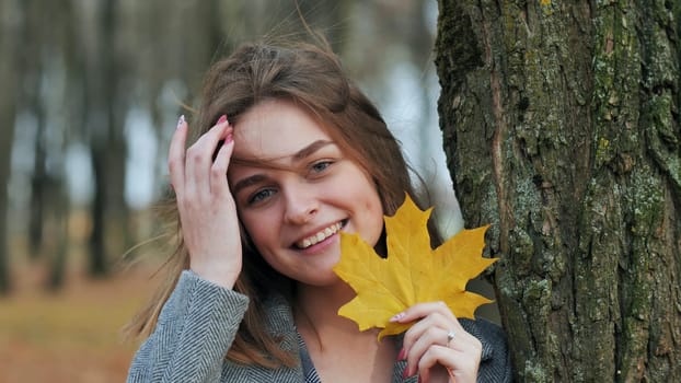 Beautiful happy woman with a smile holds an autumn yellow leaf near the face