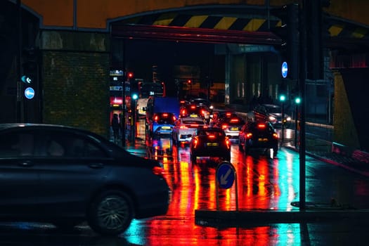 London, United Kingdom - February 01, 2019: Buses and cars stuck waiting in traffic at red light on a rainy evening near Lewisham station, bright lights reflected in wet road and pavement