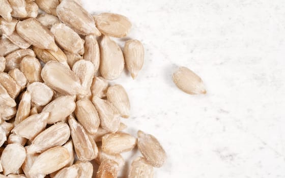 Peeled sunflower seeds on white stone board, closeup view from above, empty space right side