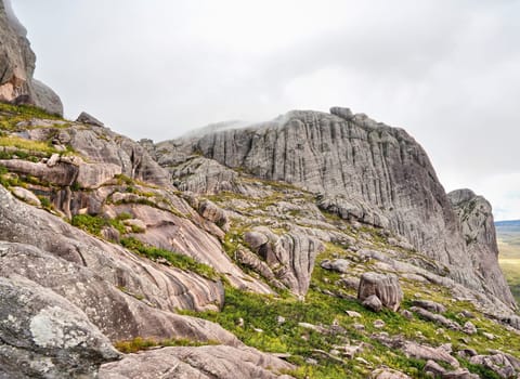 Tall rocky massif with low grass and bushes growing over stones - typical scenery seen in Andringitra during trek to Pic Boby peak
