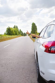 A young girl driving a car, pulls her hand out of the window and shows like