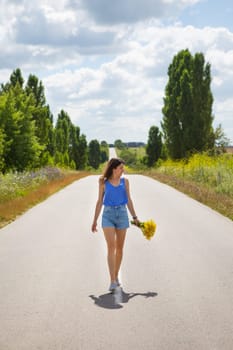 Attractive girl, posing, walking with a bouquet of yellow flowers in the middle of the asphalt road near the field, copy space for content