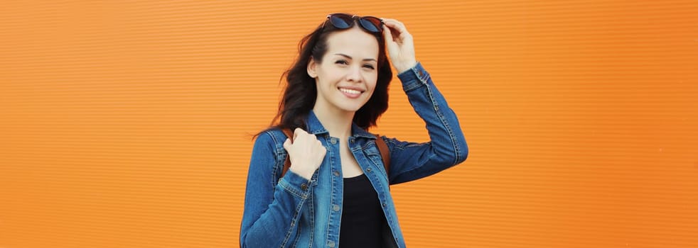 Portrait of beautiful brunette young woman smiling in sunglasses posing in the city on orange background, copy space
